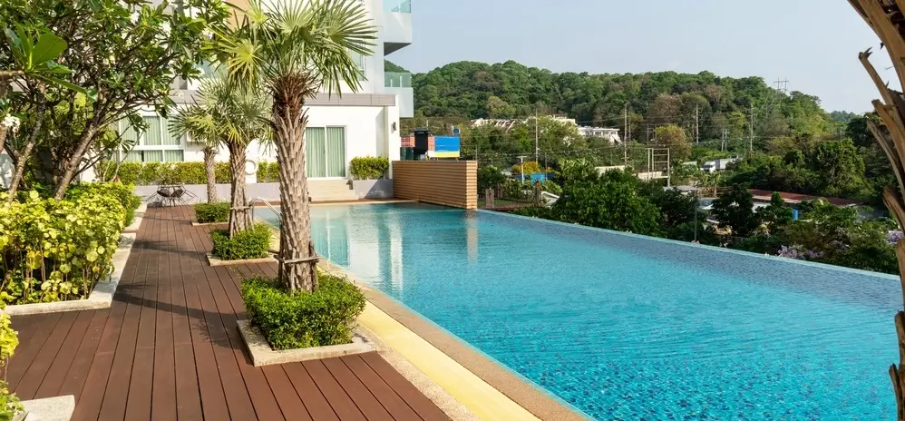 A sleek above-ground pool deck with wooden planks, palm trees, and lush greenery overlooking a scenic hilly backdrop.