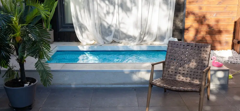 A concrete pool above ground, surrounded by palm plants and a cozy seating area.