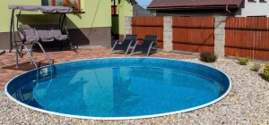 A small round fiberglass swimming pool surrounded by a cozy backyard setup with seating and landscaping.