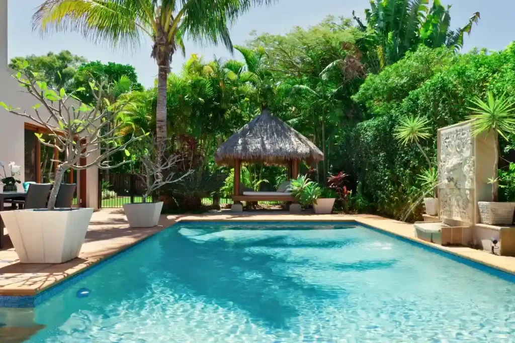 A DIY fiberglass pool surrounded by lush tropical greenery and a cozy cabana setup.