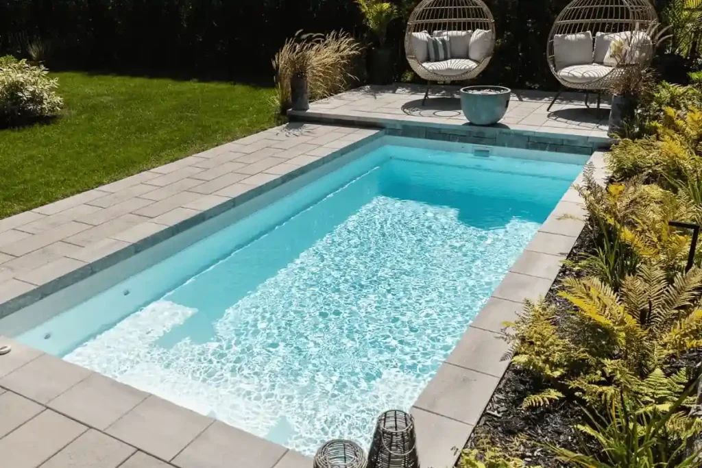 A beautifully designed fiberglass plunge pools surrounded by a landscaped garden, featuring two hanging egg chairs and potted plants, creating a serene outdoor retreat.