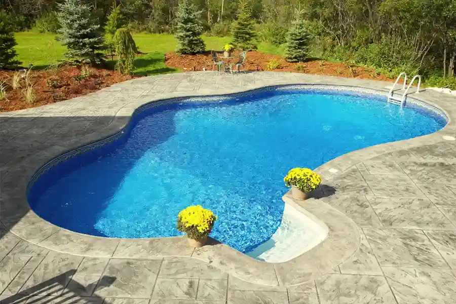 Stunning freeform concrete pool crafted by concrete pool companies near me, surrounded by stamped concrete and vibrant plants.