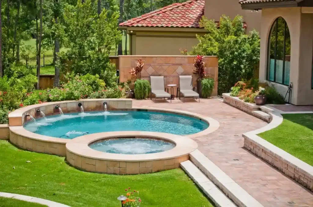 A fiberglass plunge pools with a built-in spa, surrounded by lush greenery, colorful flowers, and a stone patio in a luxurious backyard setting.