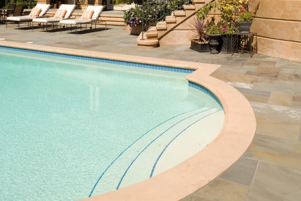 Beautiful curved concrete pool designed by concrete pool companies near me, featuring stylish stairs and surrounded by lounge chairs and greenery.