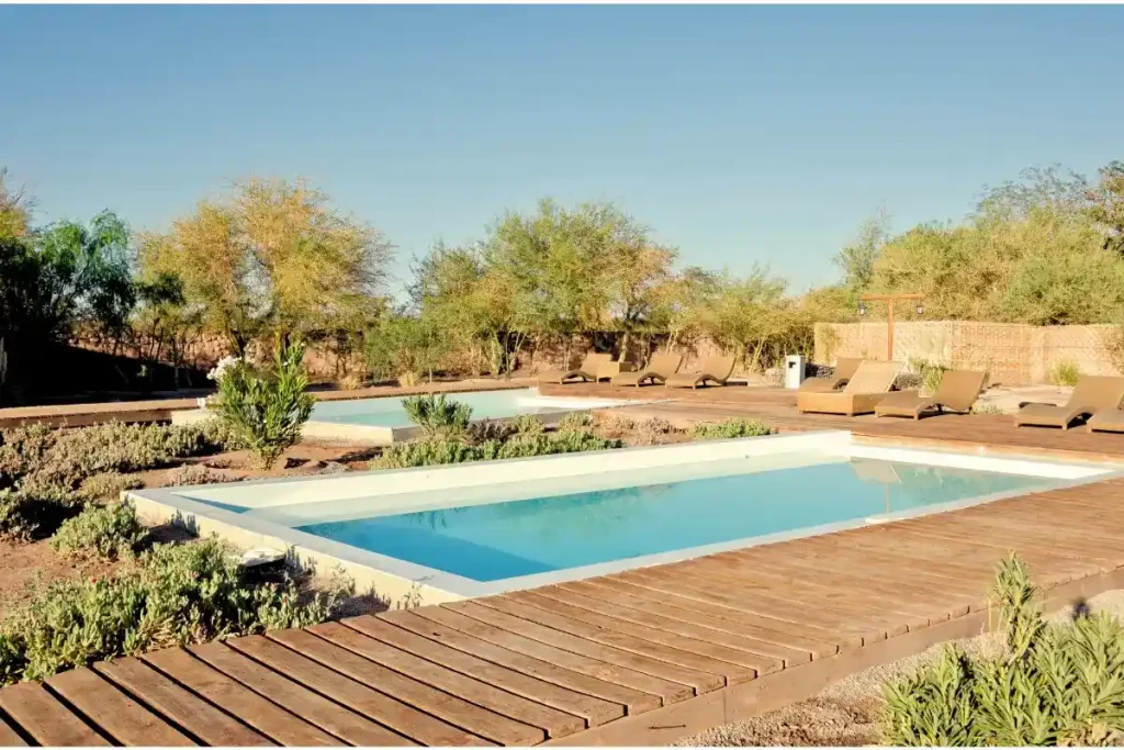 A modern fiberglass pool in Ocala with a wooden deck, surrounded by desert landscaping and sun loungers.