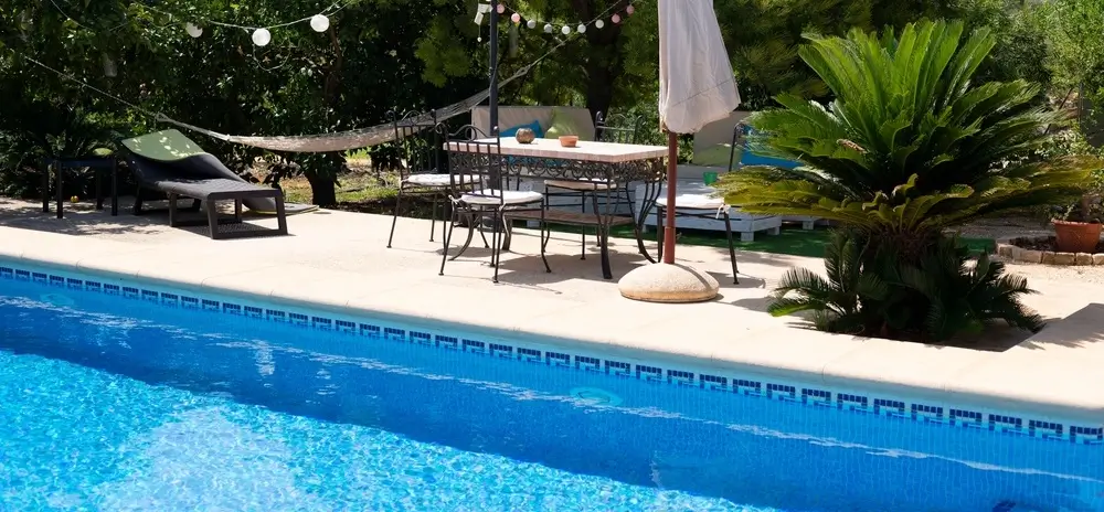 A serene backyard showcasing creative concrete pool ideas with outdoor furniture, lush greenery, and decorative string lights.