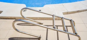 A detachable above-ground pool deck ladder placed near a blue swimming pool on a tiled deck, ready for maintenance or repair.