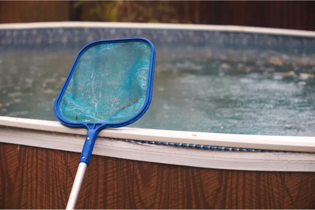 Pool skimmer resting on the edge of an above ground pool base during cleaning.