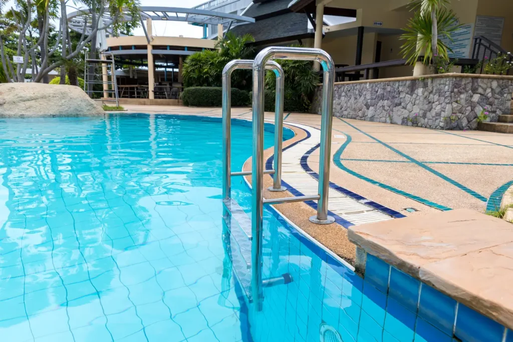 A shiny stainless steel above-ground pool deck ladder with multiple steps, leading into a clear blue swimming pool.