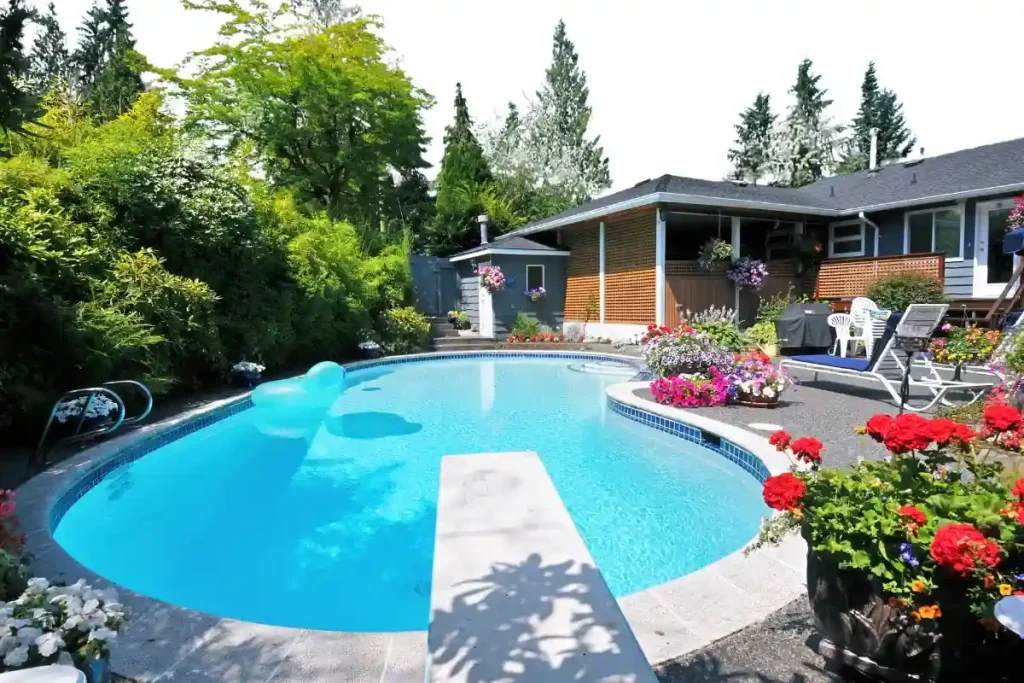 A kidney-shaped fiberglass pool in Ocala, nestled in a vibrant backyard with colorful flowers and a diving board.