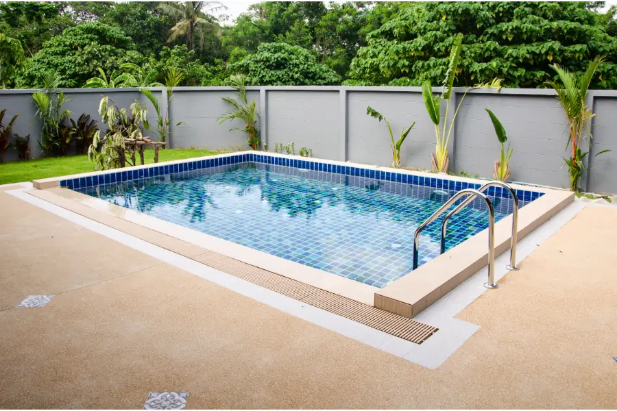 A tropical-inspired swimming pool with lush greenery and blue-tiled flooring, designed for a relaxing ambiance.