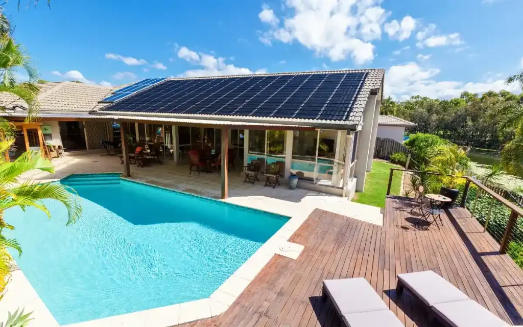 A beautiful swimming pool in Florida with a modern deck, lounge chairs, and a house with solar panels.