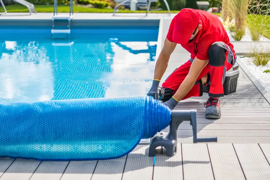 A pool installer in a red uniform rolling out a pool cover for maintenance.